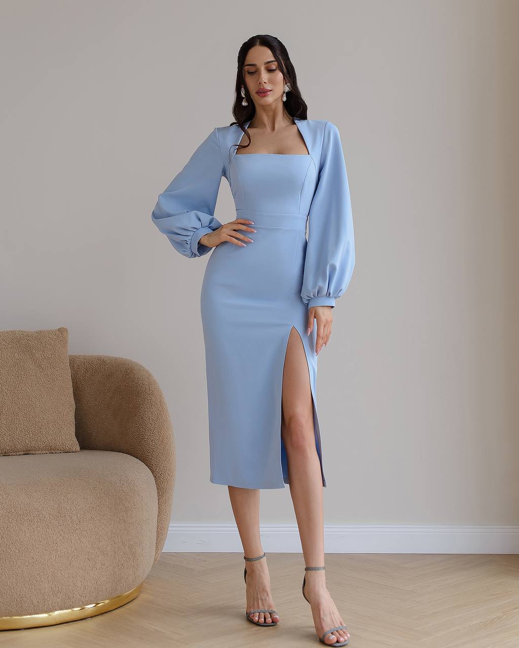 Woman wearing a light blue dress with a slit standing in a room with a beige couch.
