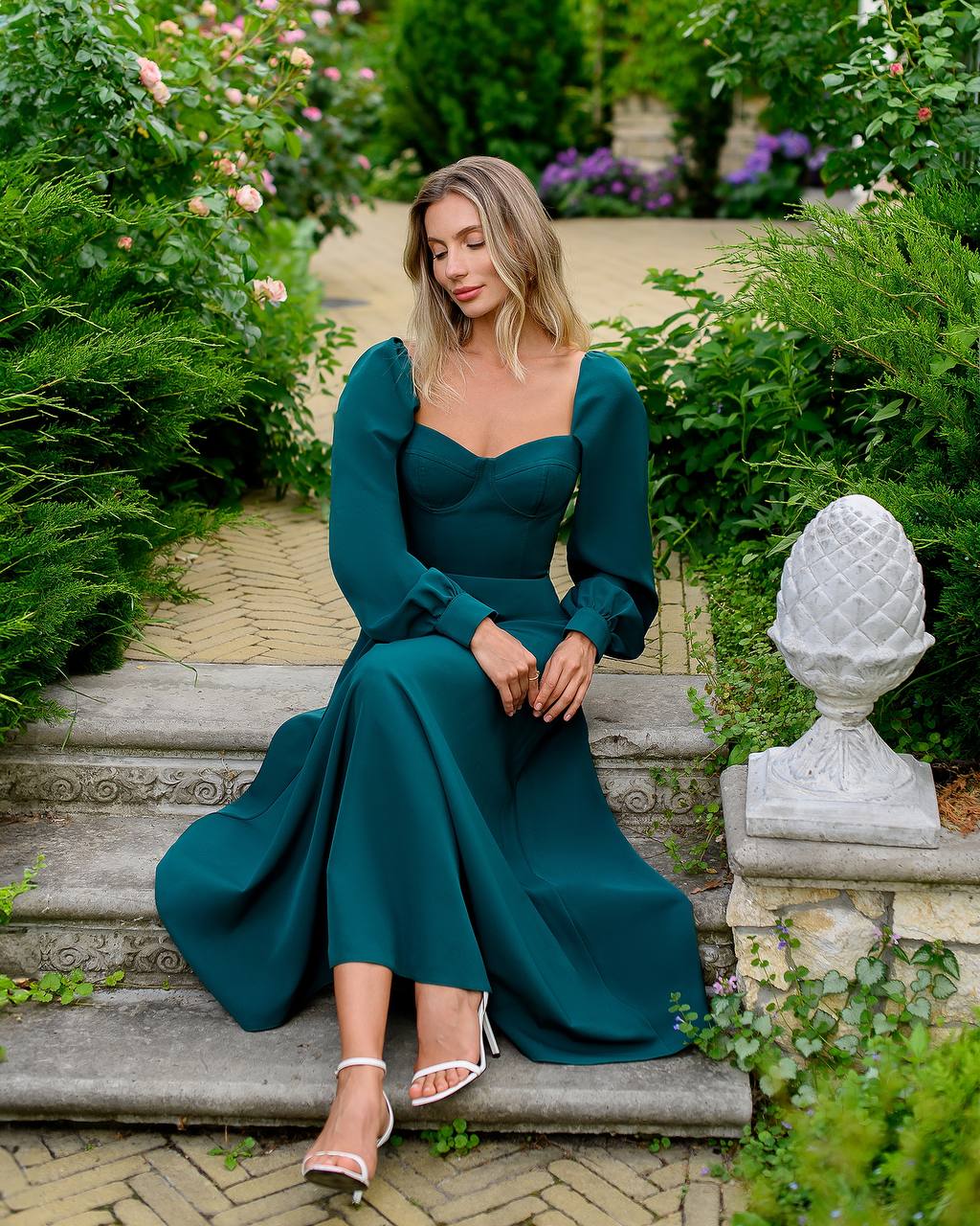 Woman in a teal dress sitting on stone steps in a garden