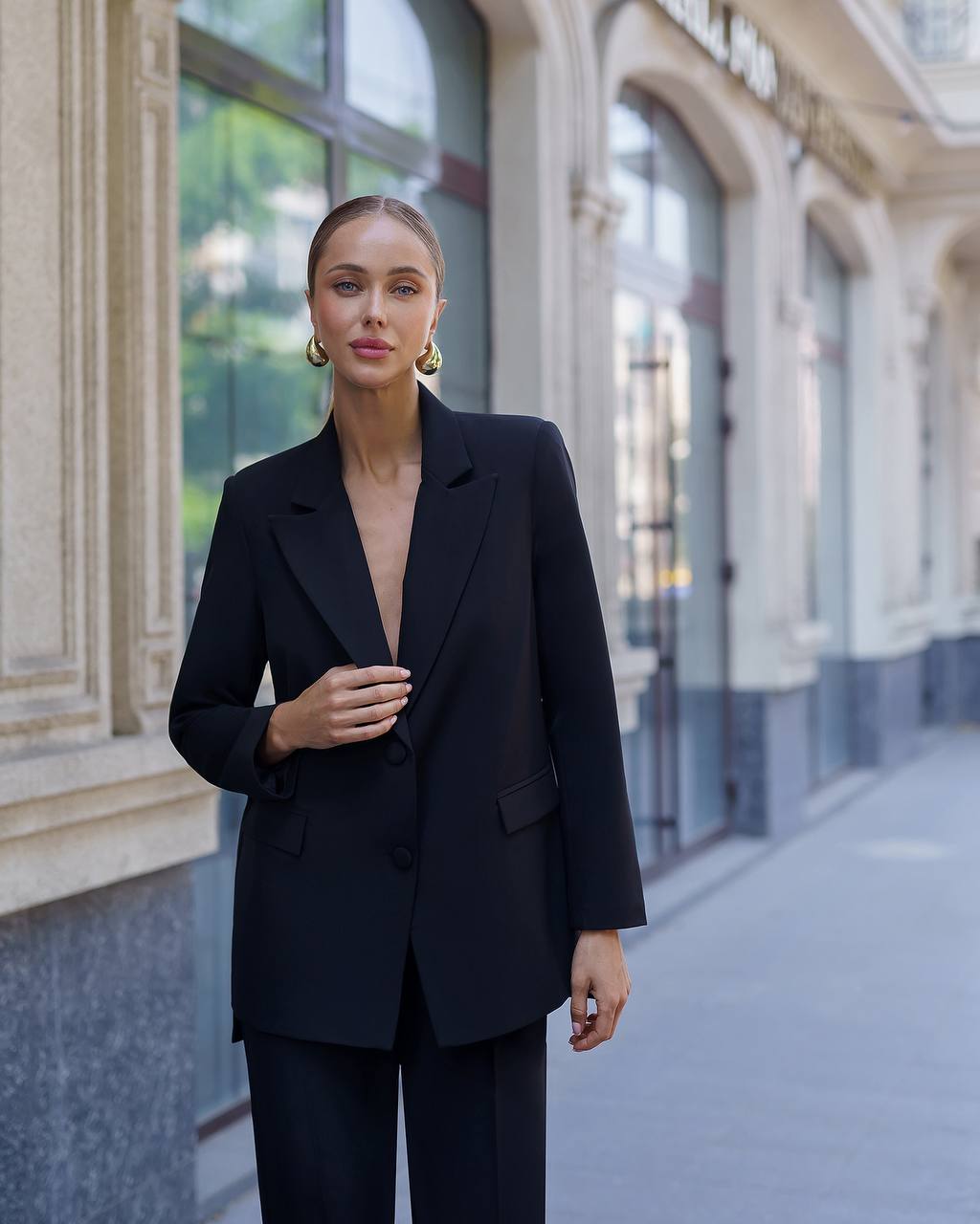Woman wearing a black suit standing on a city street.