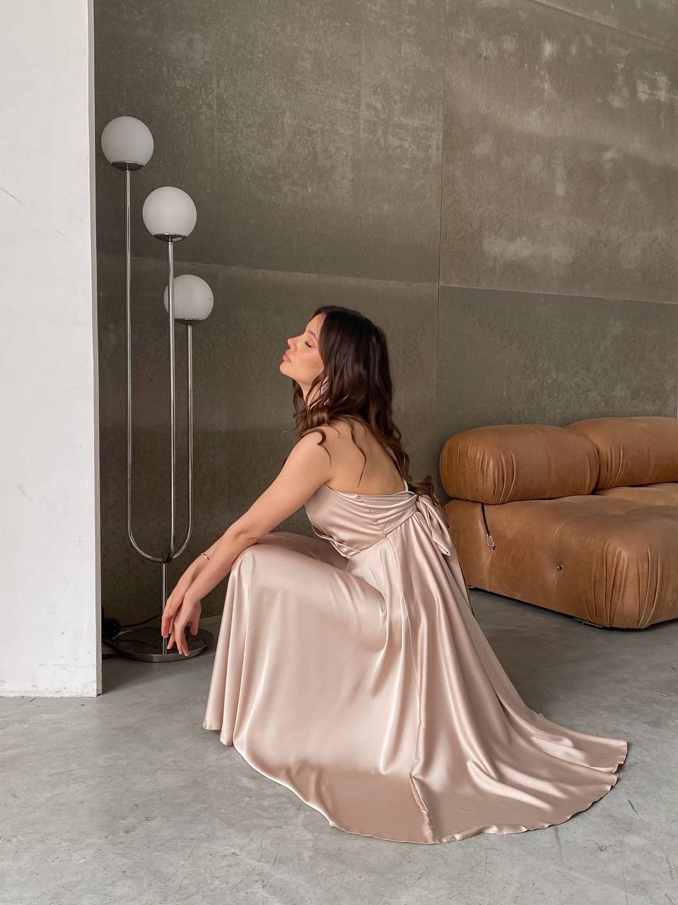 Woman in a flowing dress sitting on the floor in a modern interior setting.