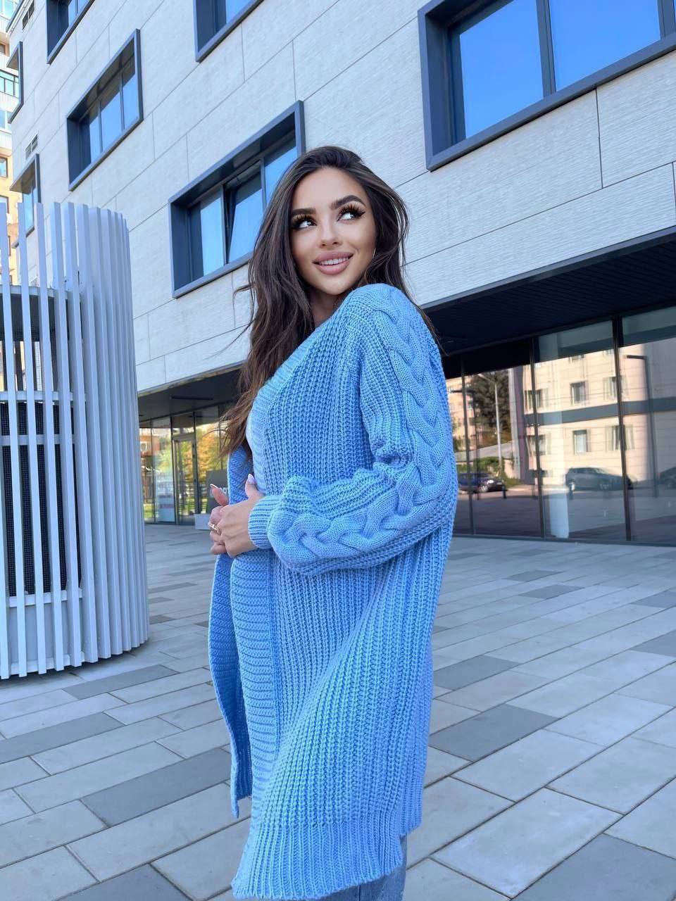Woman wearing a blue knitted cardigan standing in front of a modern building.