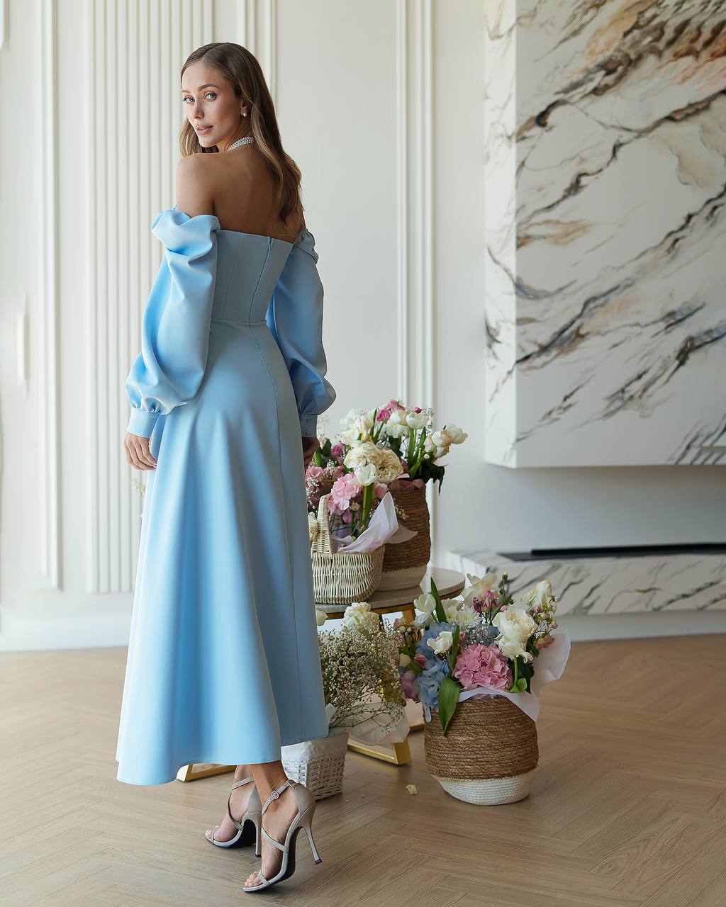 Woman in a light blue dress standing in a room with floral arrangements.