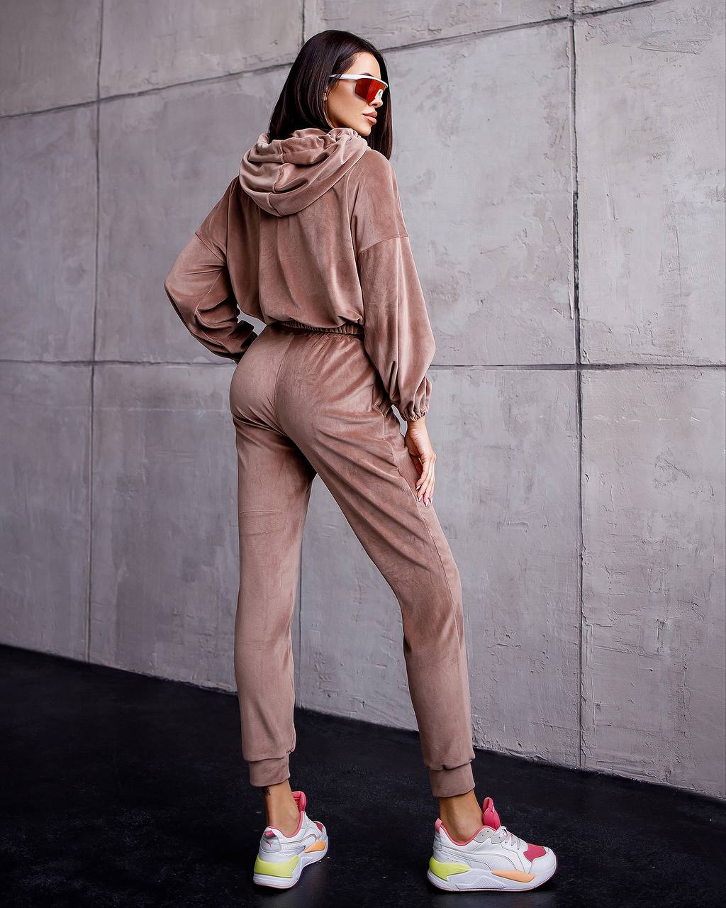 Woman wearing a beige tracksuit against a gray concrete wall