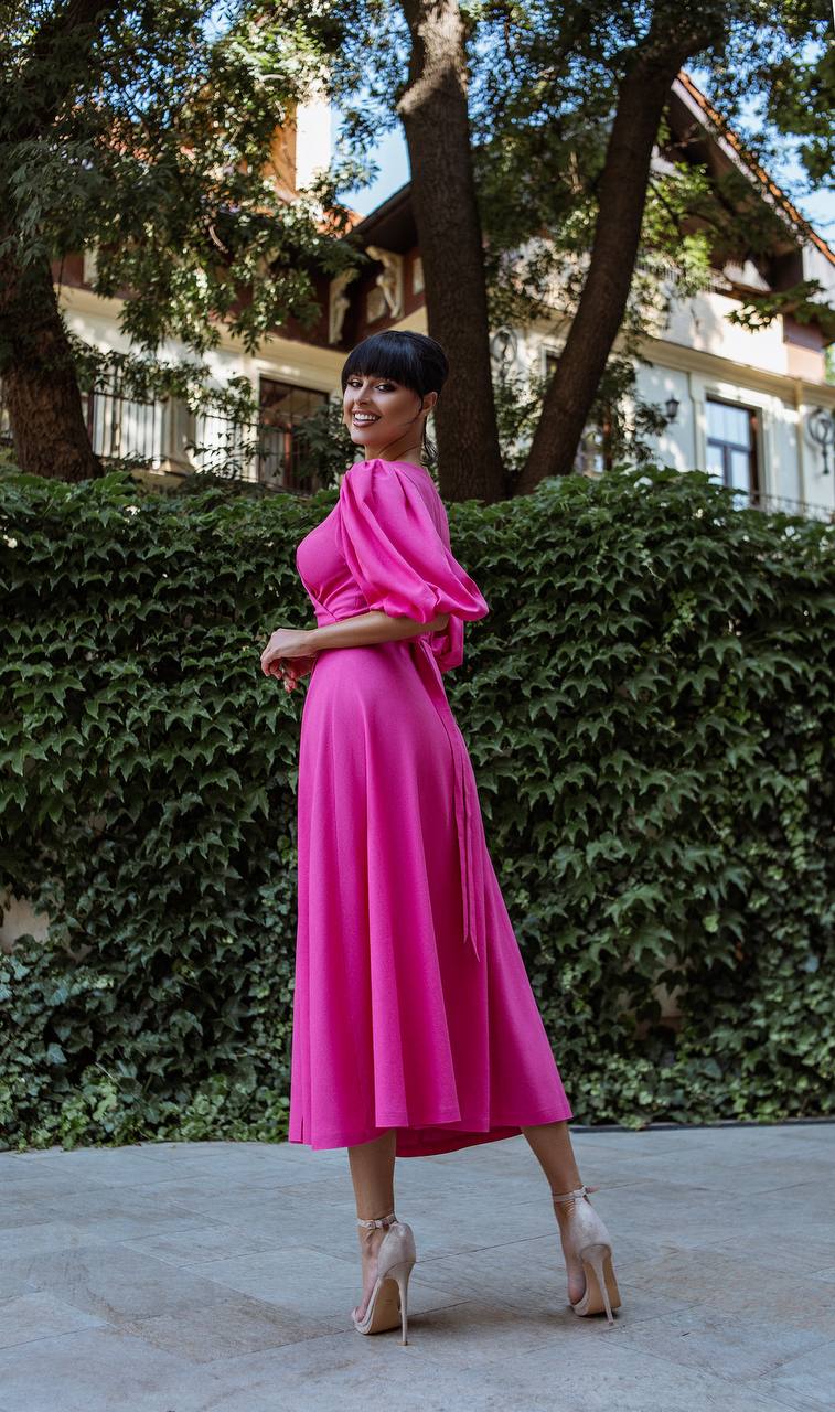 Woman in a bright pink dress standing outdoors with greenery in the background