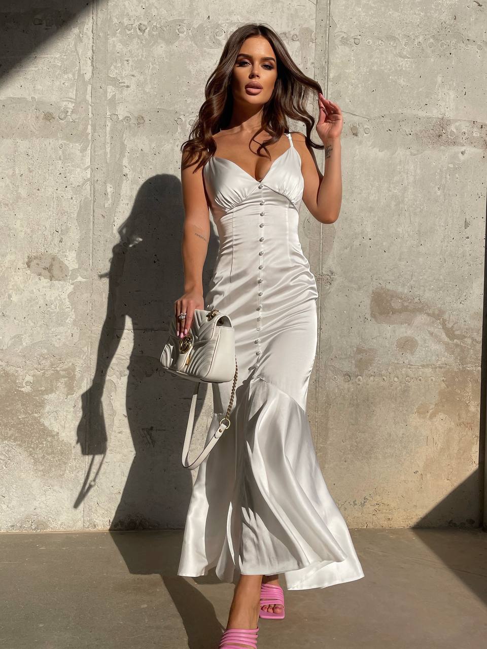 Woman in a white satin dress standing against a concrete wall.