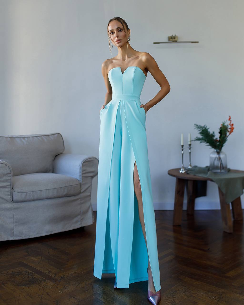 Woman in a light blue strapless gown with a high slit standing in a room.