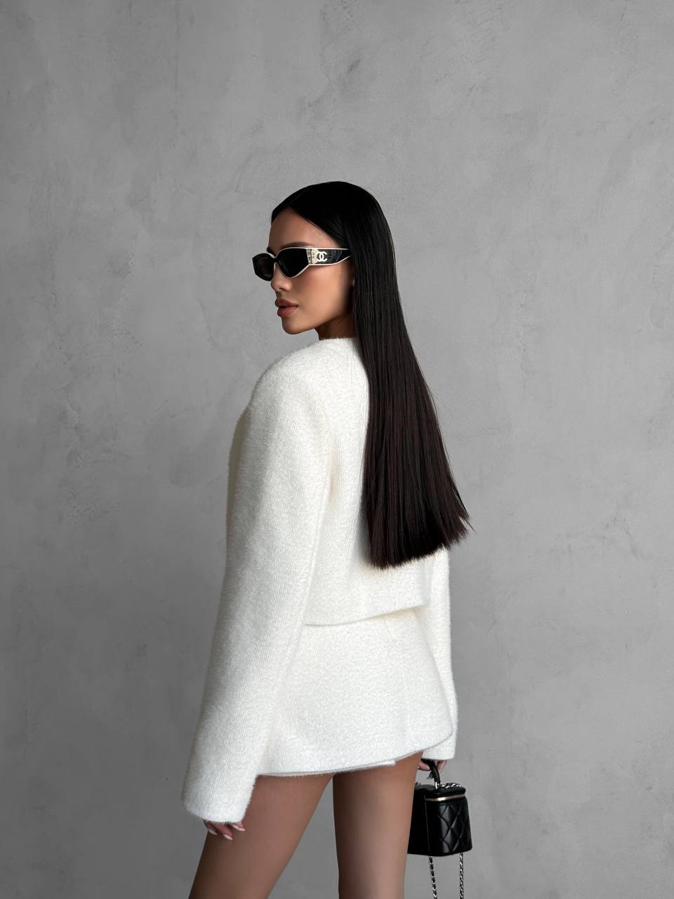 Woman in a white outfit with sunglasses against a gray background