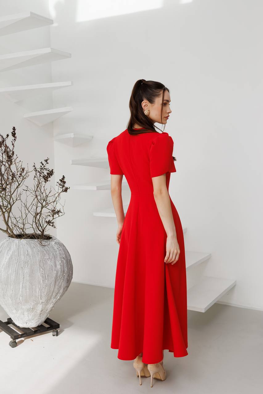 Woman in a red dress standing in a minimalistic room with white walls and a large vase.