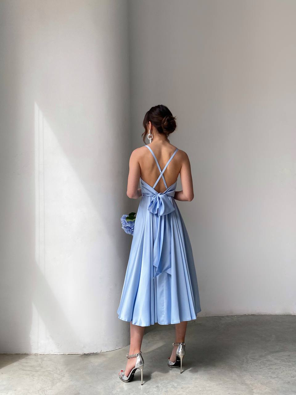 Woman in a light blue dress standing against a plain wall.