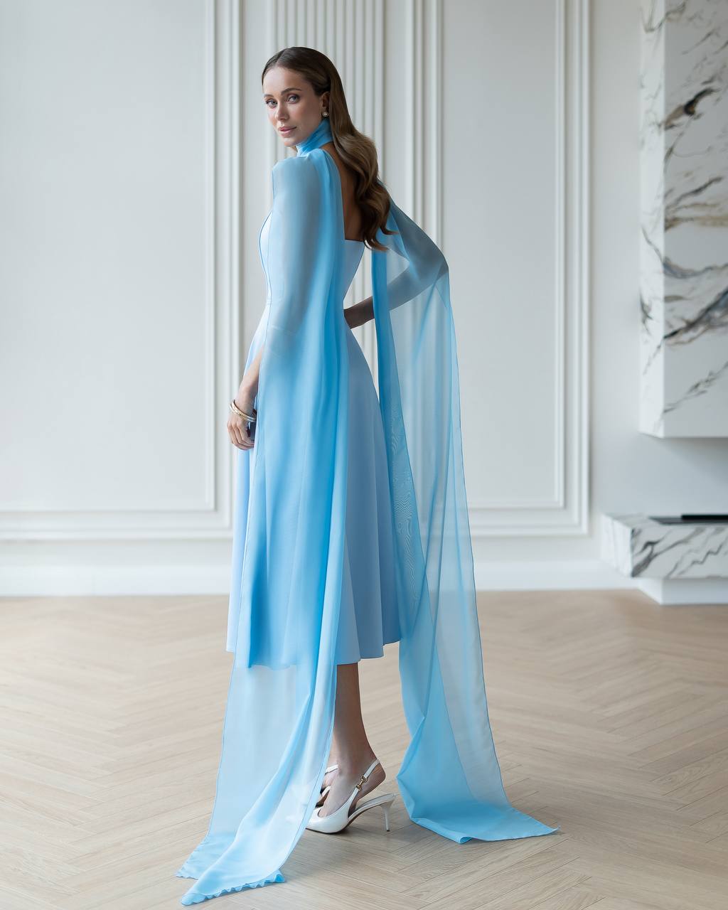 Woman wearing a light blue dress with a sheer overlay in an elegant room.