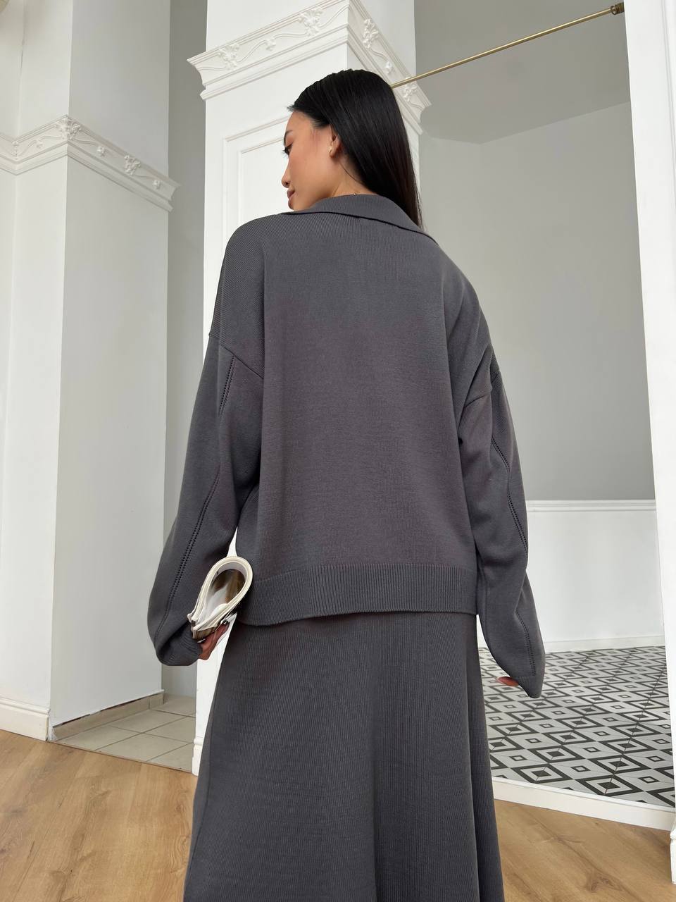 Person wearing a gray outfit in a room with white walls and wooden floor.