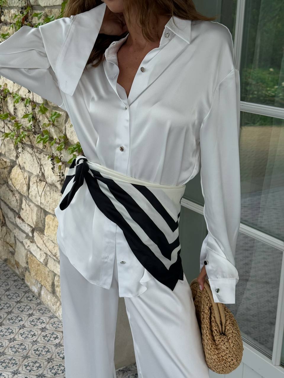 Woman wearing a white blouse with a black and white striped tie, standing outdoors.