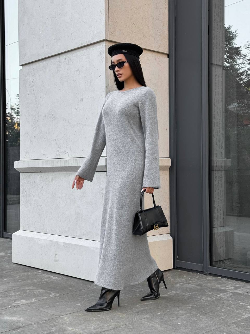 Woman in a long gray dress standing outside a building.