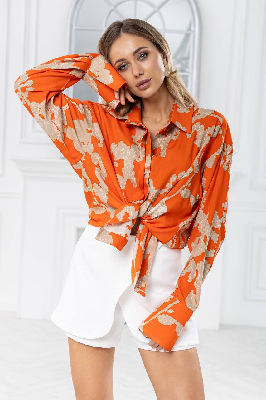 Woman wearing an orange and beige patterned blouse with a white background