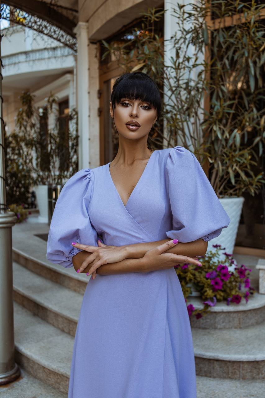 Woman in a lavender dress standing outdoors with decorative elements in the background