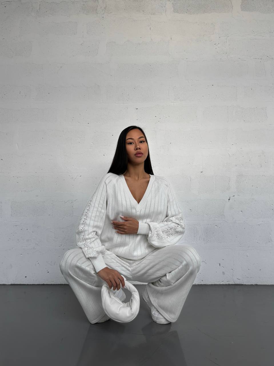 Person wearing a white outfit sitting on a white stool against a white wall.