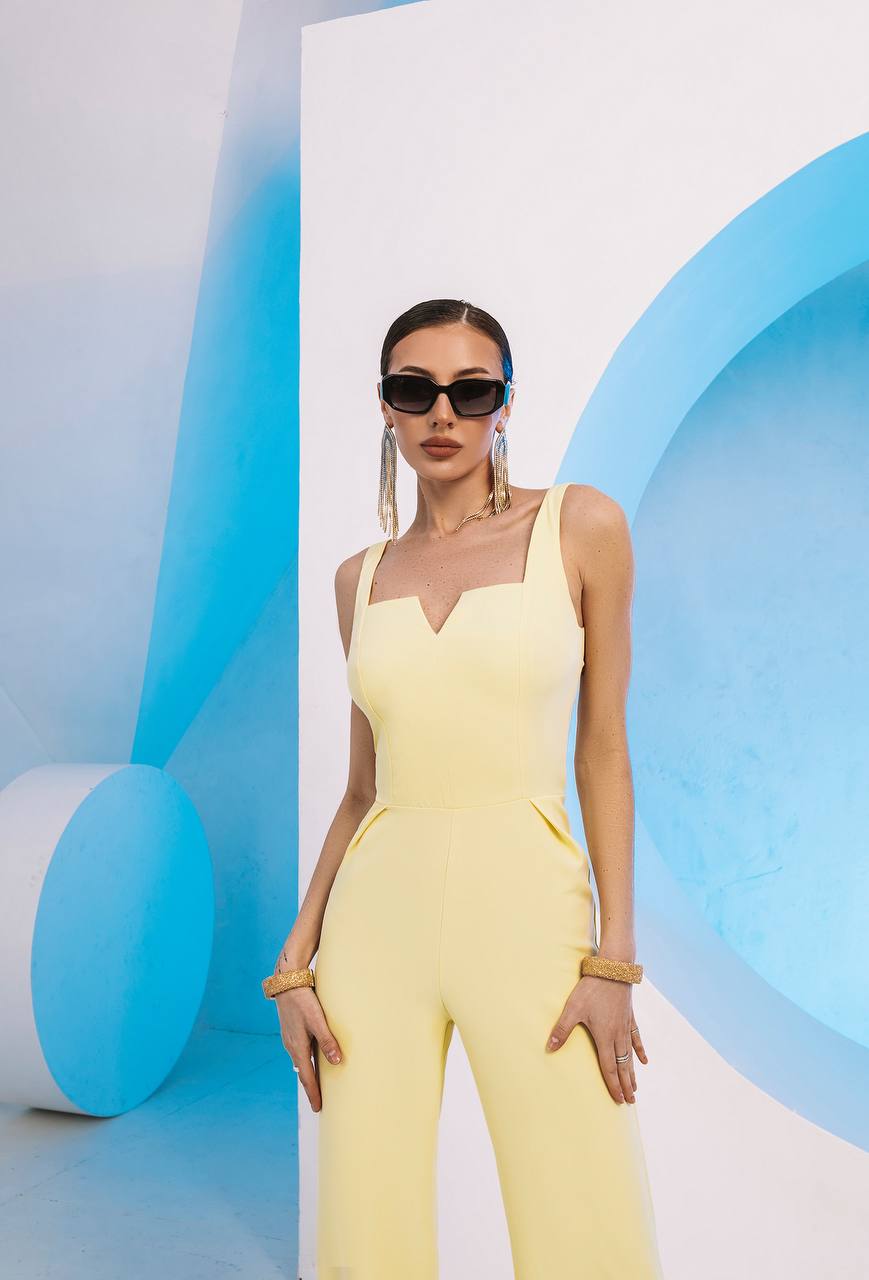 Woman in a yellow jumpsuit standing against a modern, abstract background