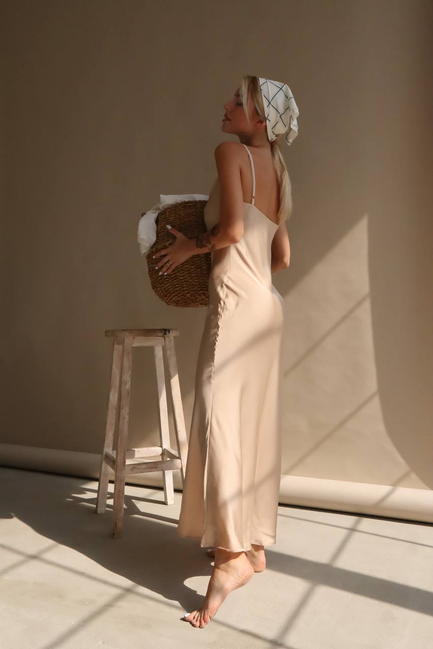 Woman in a beige slip dress holding a woven basket in a softly lit room.