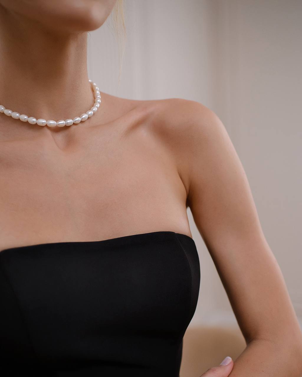 Pearl necklace worn by a person in a black strapless dress against a neutral background