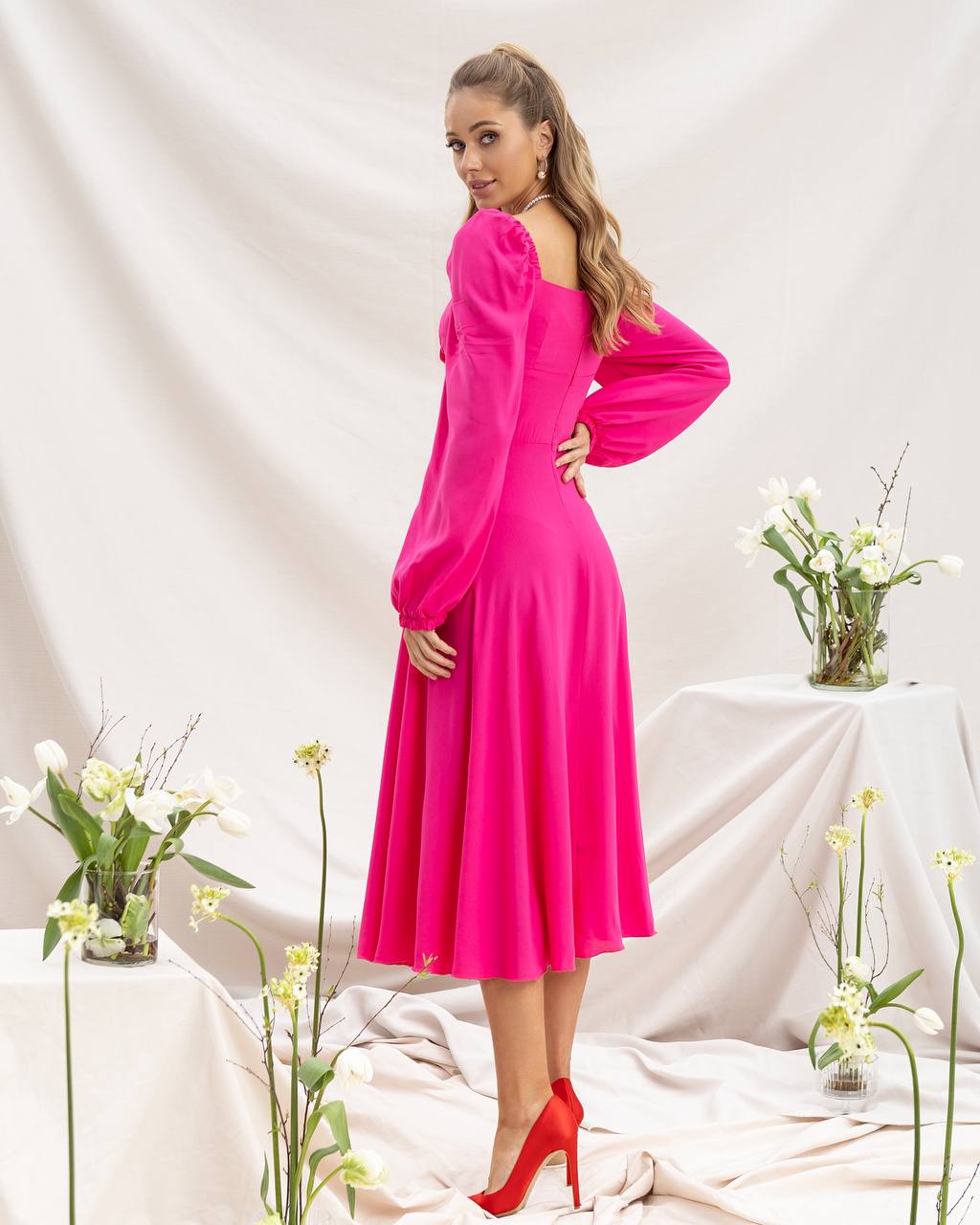 Woman in a bright pink dress standing in a decorated room with flowers.