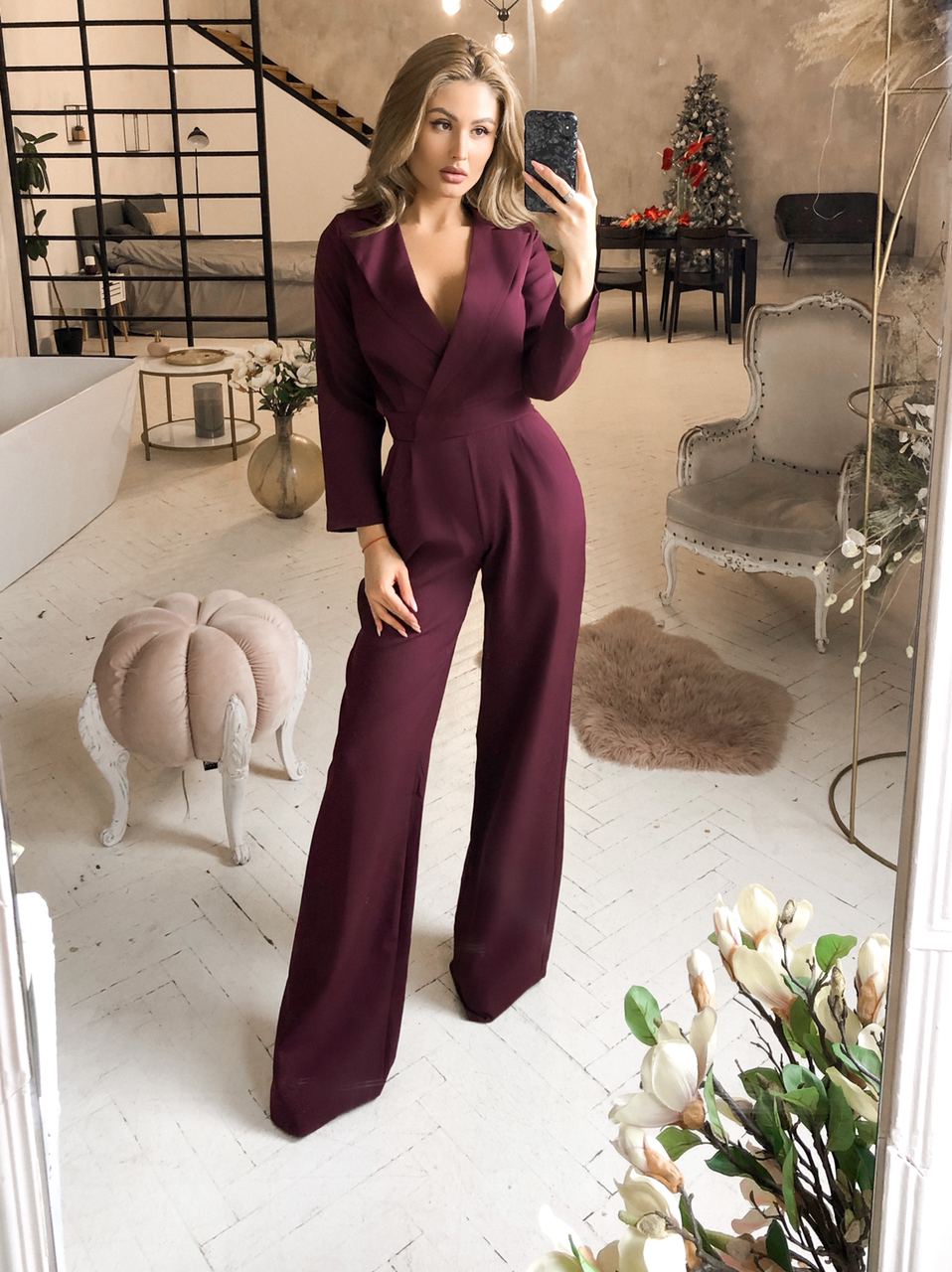 Woman taking a mirror selfie wearing a burgundy jumpsuit in a stylish room.