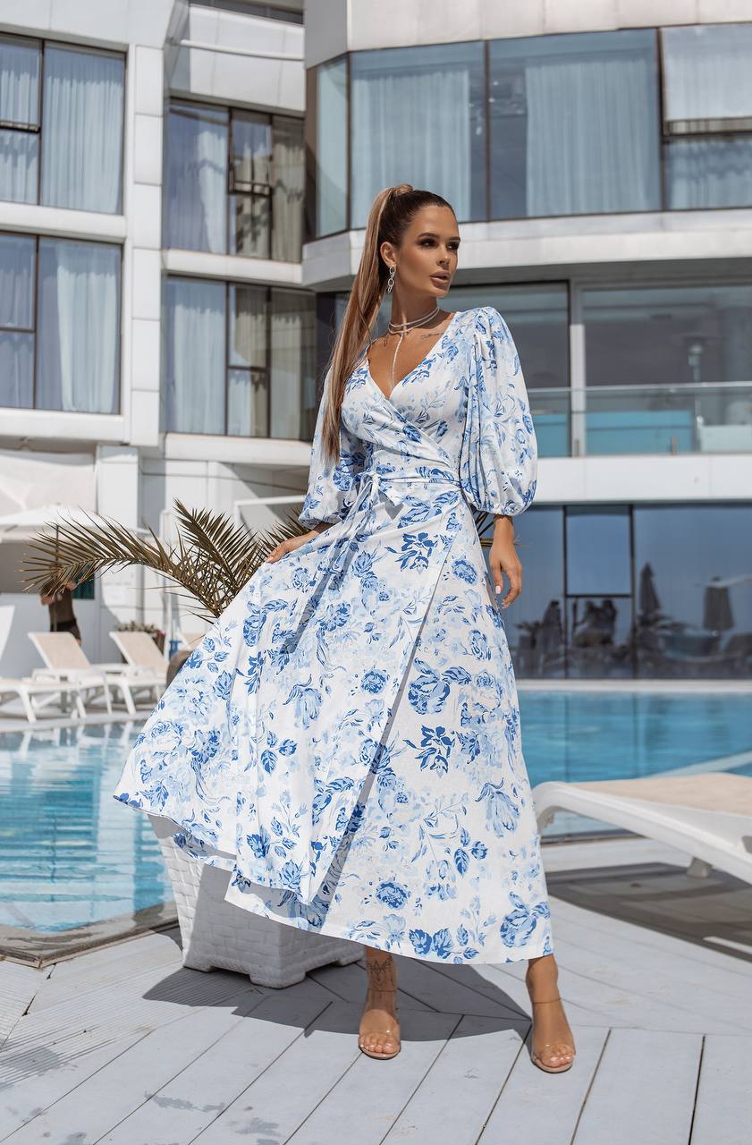 Woman in a blue floral dress standing by a pool with modern building in the background