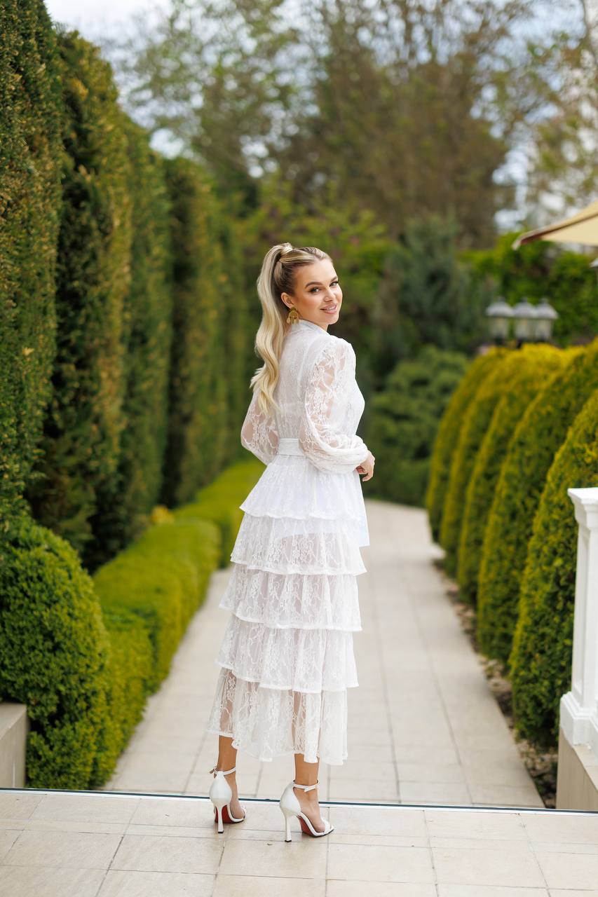 Woman in a white dress standing in a garden with manicured hedges.