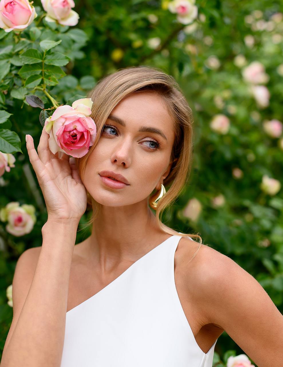 Woman holding a pink rose in front of a floral background