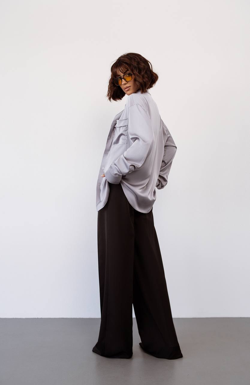 Person wearing a light gray oversized shirt and dark pants against a white background