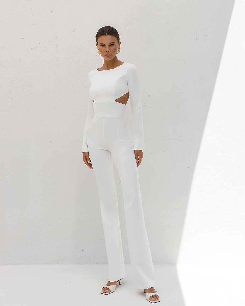 Woman wearing a white outfit with cut-out design on a plain background