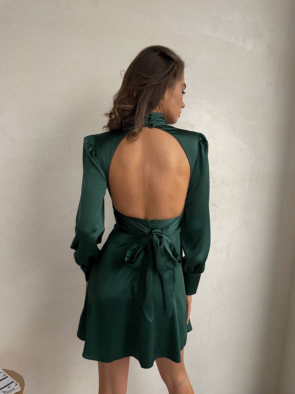 Woman wearing a green open-back dress against a neutral background