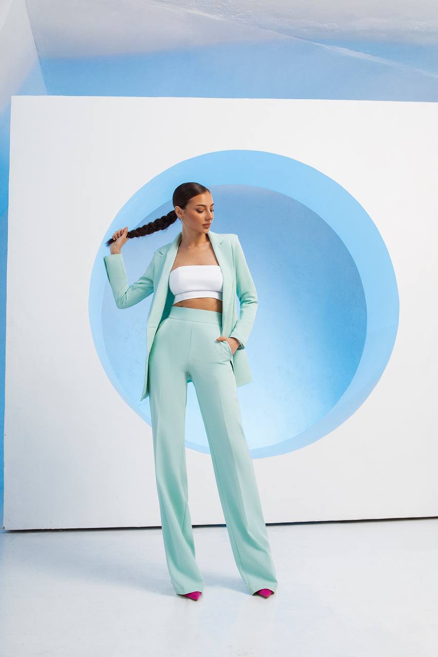 Woman in a light green outfit standing in front of a blue circular design on a white background