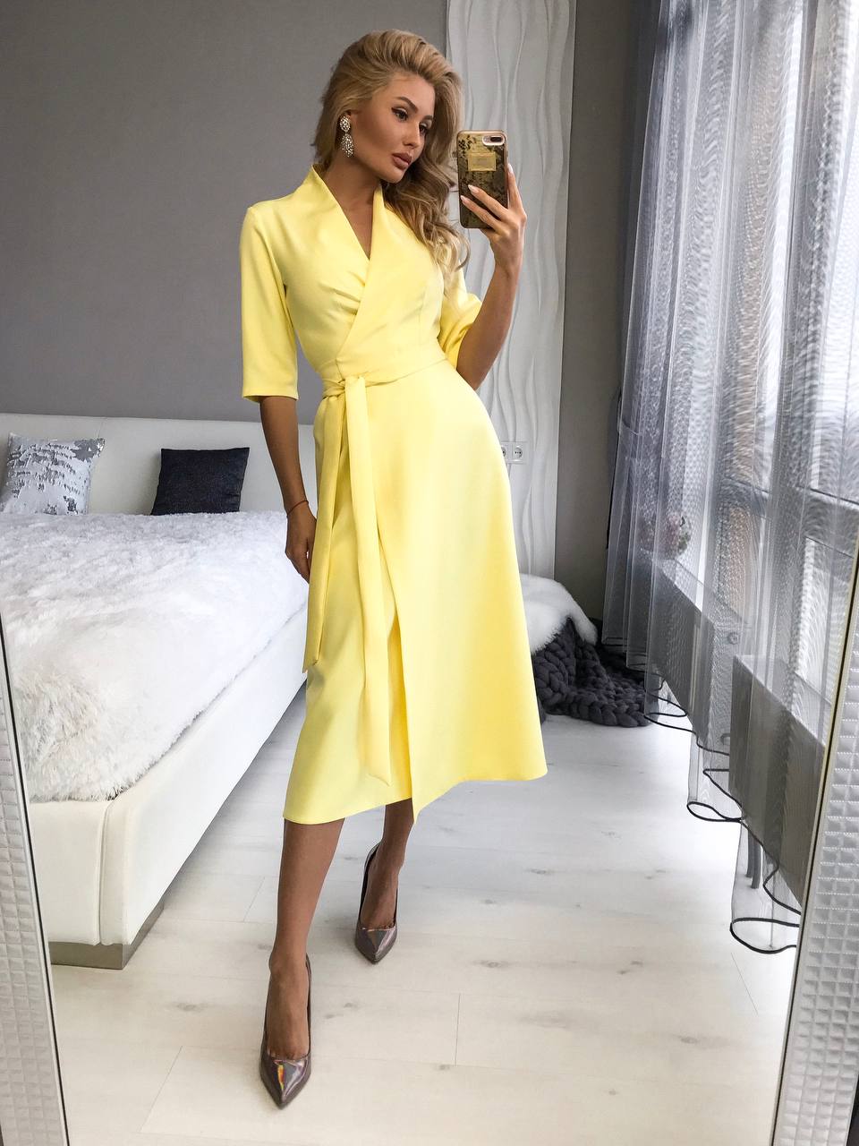 Woman in a yellow dress taking a mirror selfie in a bedroom.