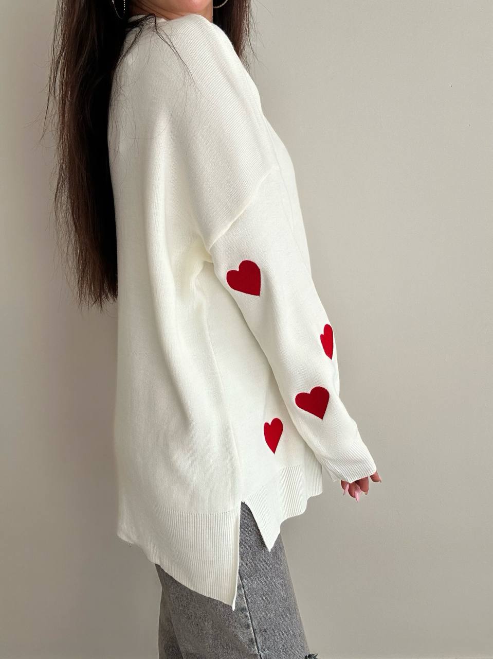 White sweater with red heart patterns worn by a person on a plain background
