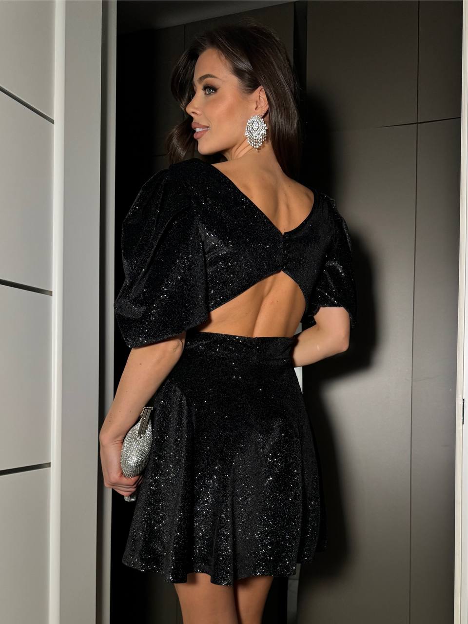 Woman in a black sequin dress standing against a neutral wall.