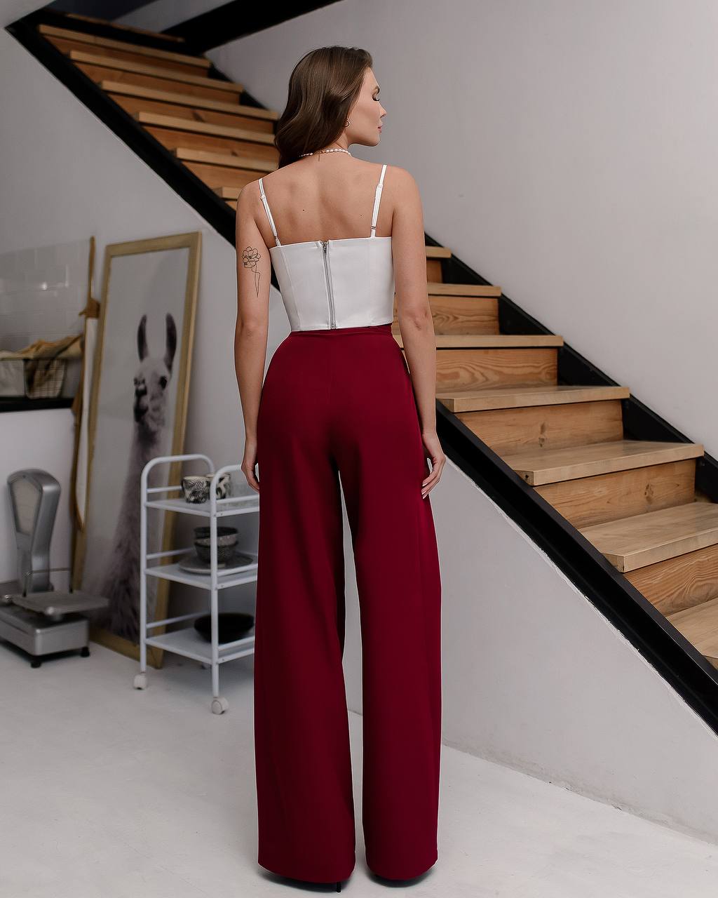 Woman in a white top and red pants standing on a staircase in a modern interior setting.