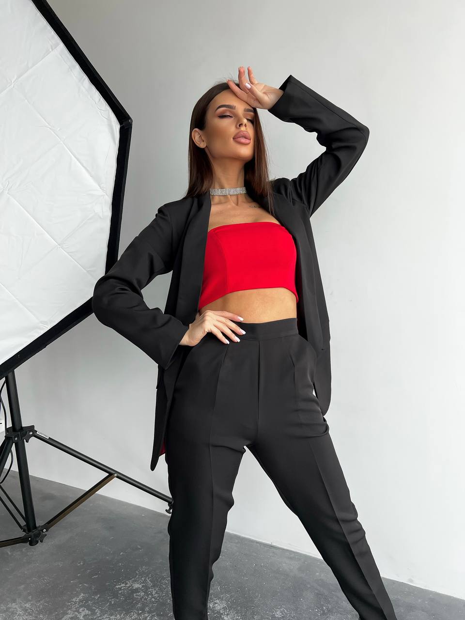 Woman in black suit with red top posing in a studio setting