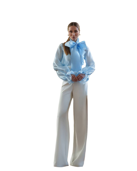 Woman wearing a white blouse with a blue bow and white pants on a white background