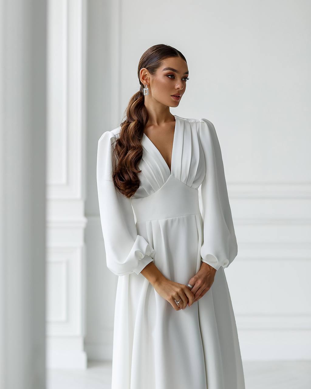 Woman wearing a white dress with long sleeves in a minimalistic setting