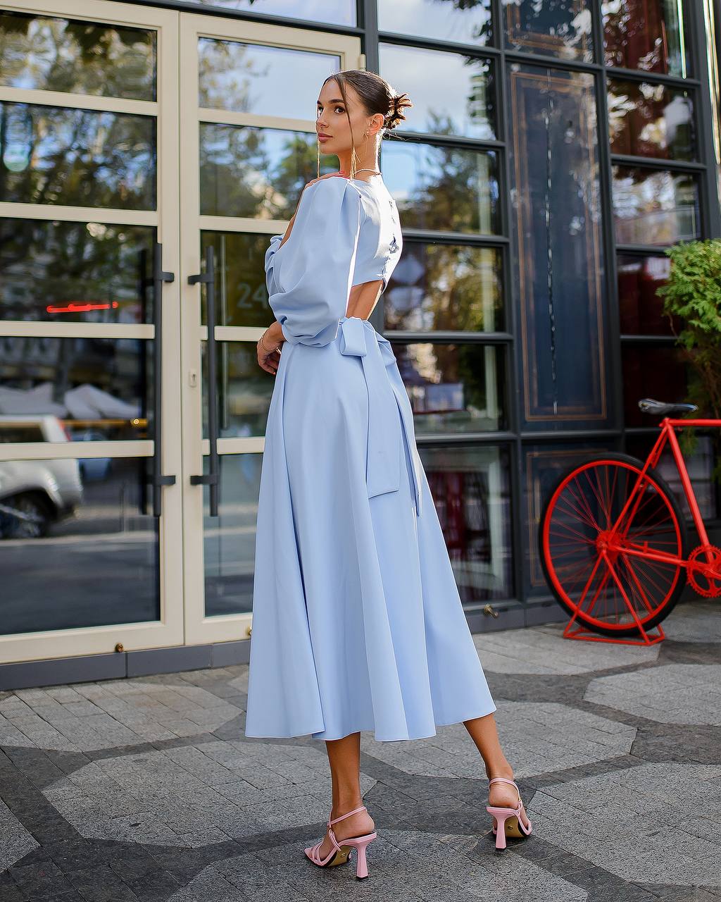Woman in a light blue dress standing outdoors with a bicycle in the background