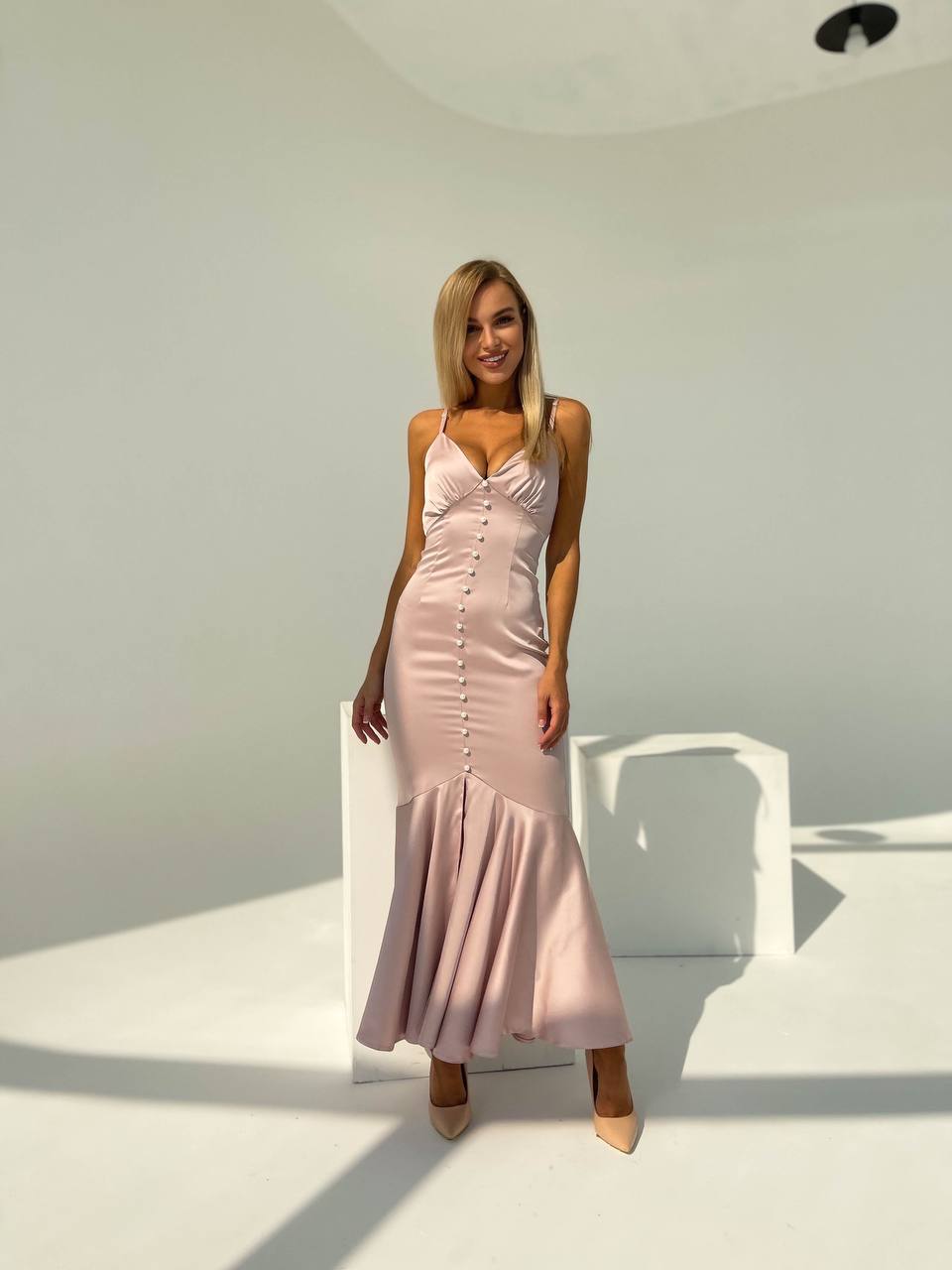 Woman wearing a pink dress standing in a minimalistic room with white walls and furniture.