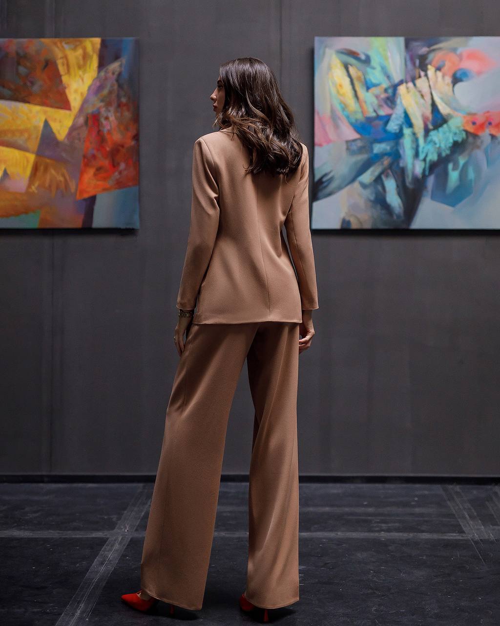Woman in a beige suit standing in front of abstract paintings in an art gallery.