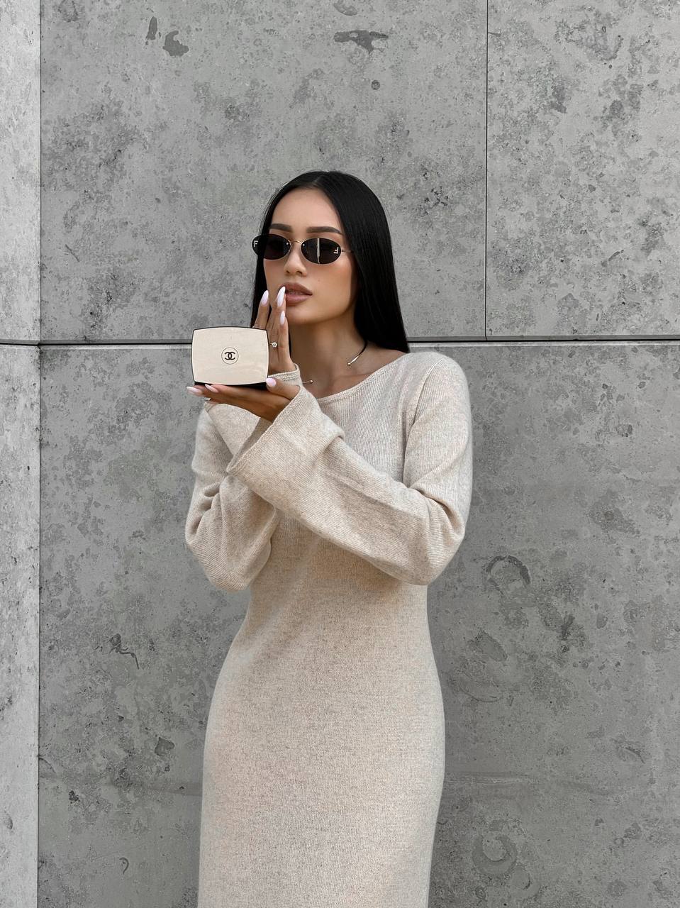 Woman in a beige dress holding a small box against a gray concrete wall