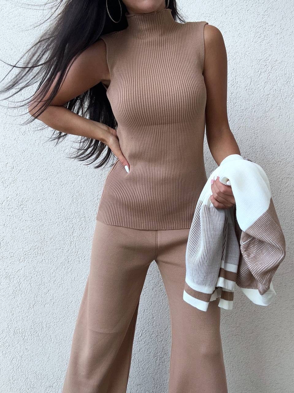 Woman wearing a beige sleeveless top and pants holding a white towel.