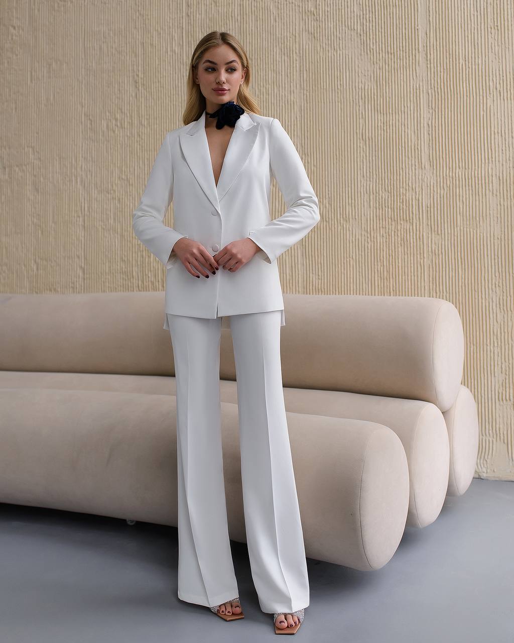 Woman wearing a white suit standing in a modern room with beige sofa and wall.