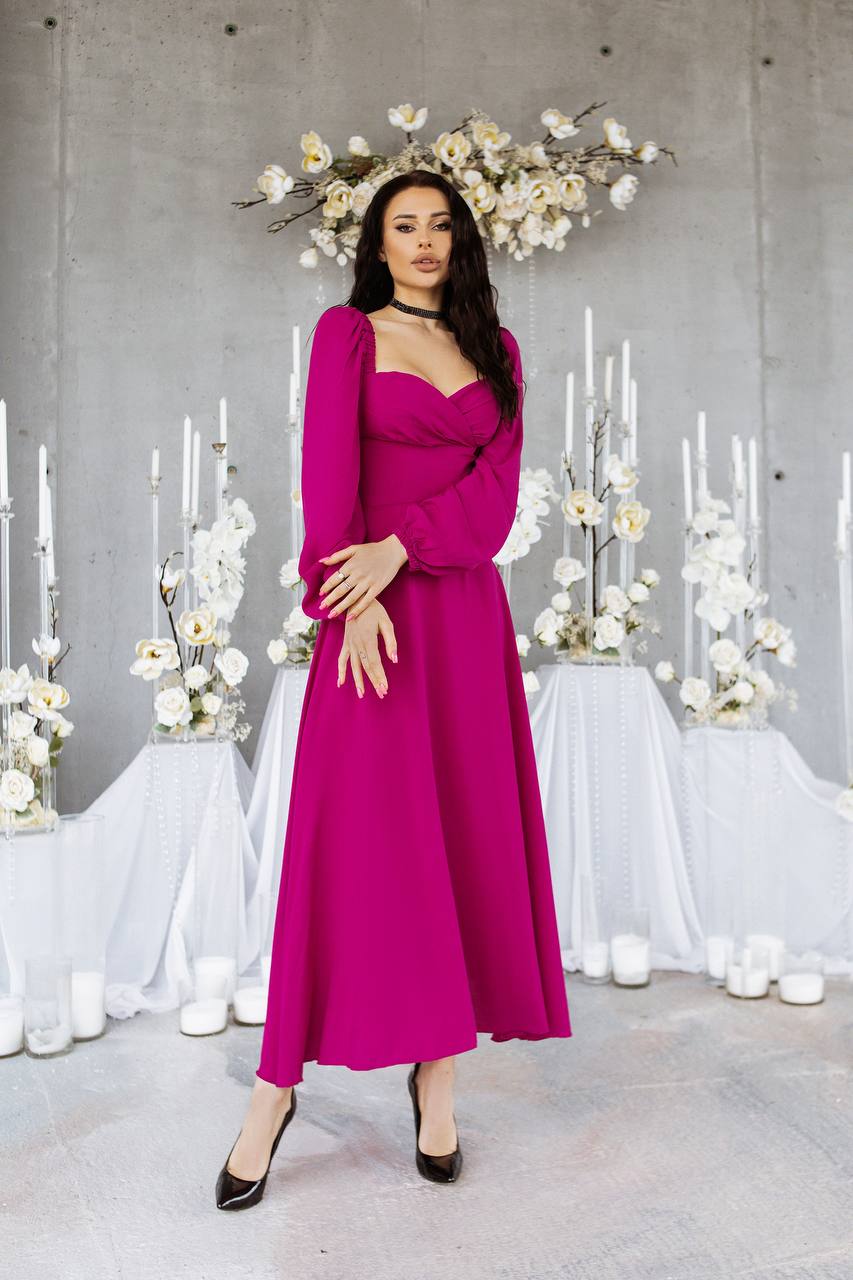 Woman in a pink dress standing in front of a decorative floral arrangement and candles.