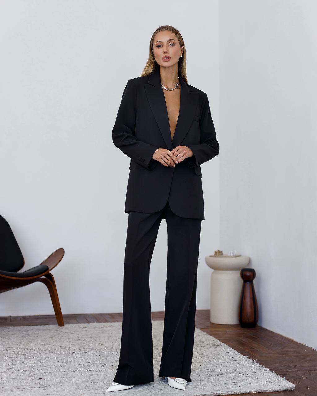 Woman wearing a black suit standing in a minimalistic room.