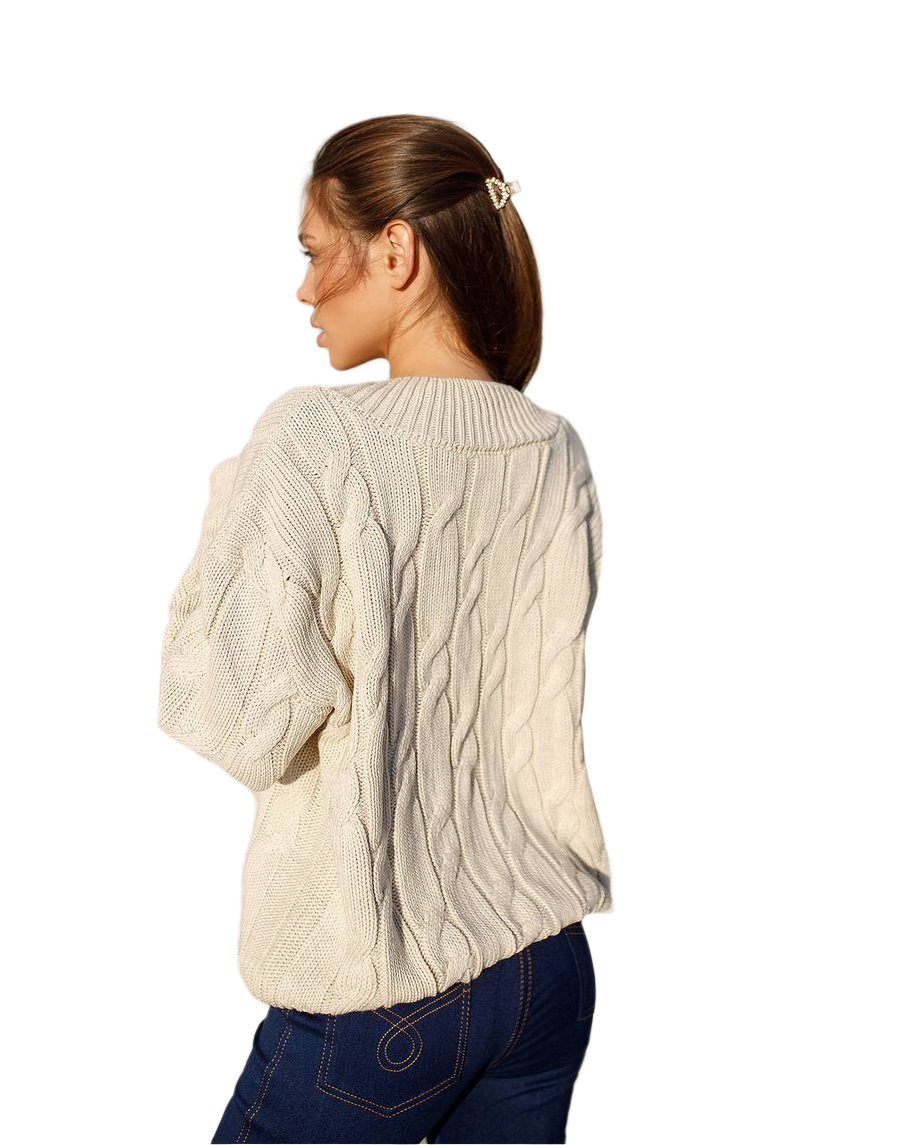 Woman wearing a cream cable knit sweater on a white background