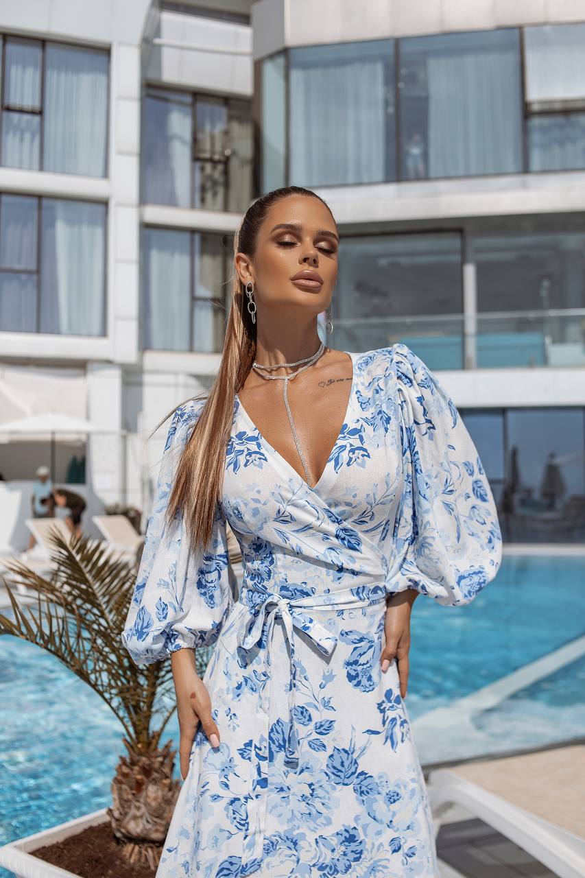 Woman in a blue floral dress standing by a pool with a building in the background