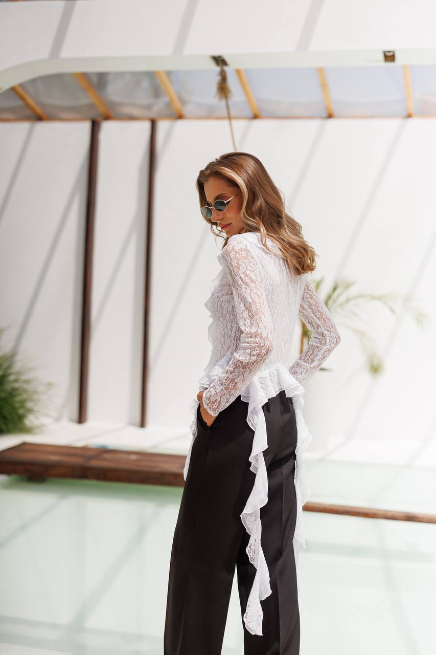 Woman wearing a white lace top and black pants in front of a white airplane.
